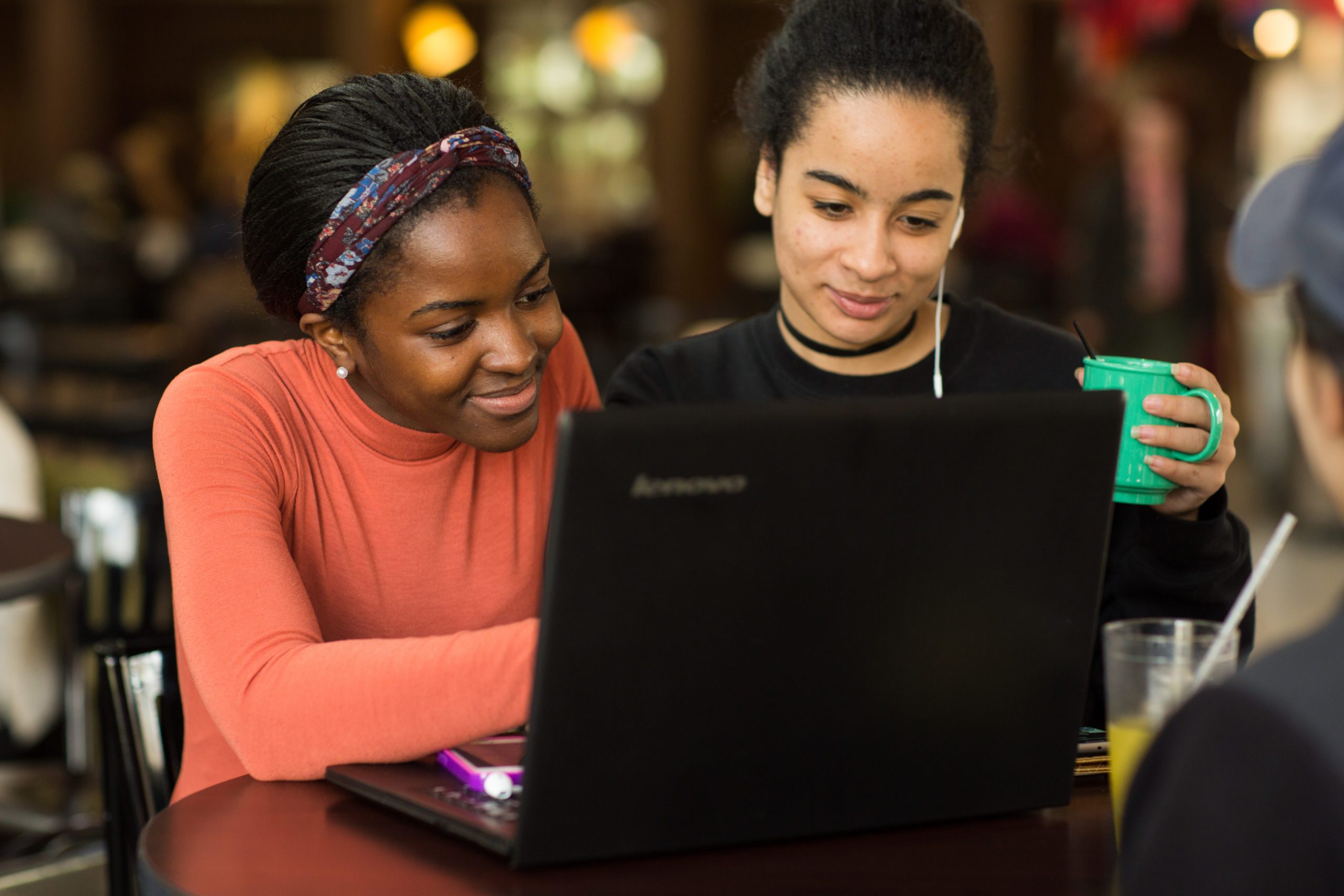 Two female students sitting at a desk viewing the screen of one laptop.