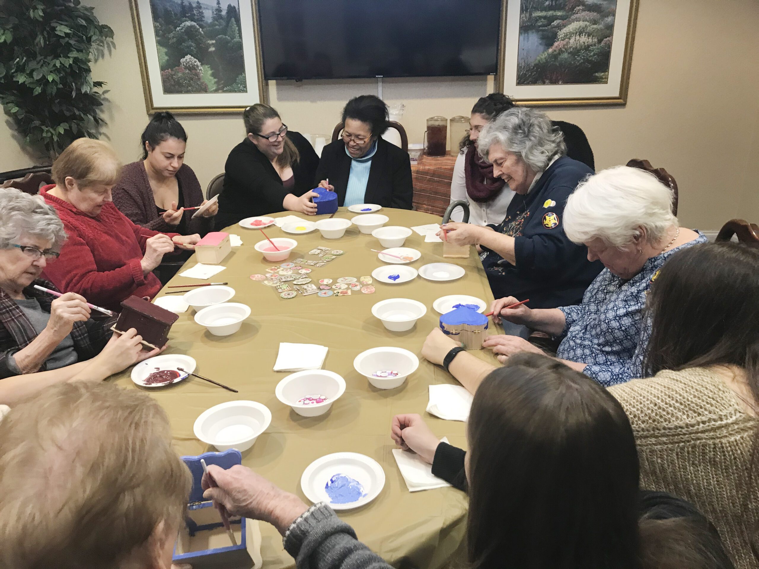 Large group seated at a table working on crafts, including students and participants at an assisted living facility