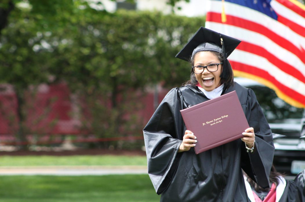 A female in a black graduation gown holding a burgundy diploma cover.