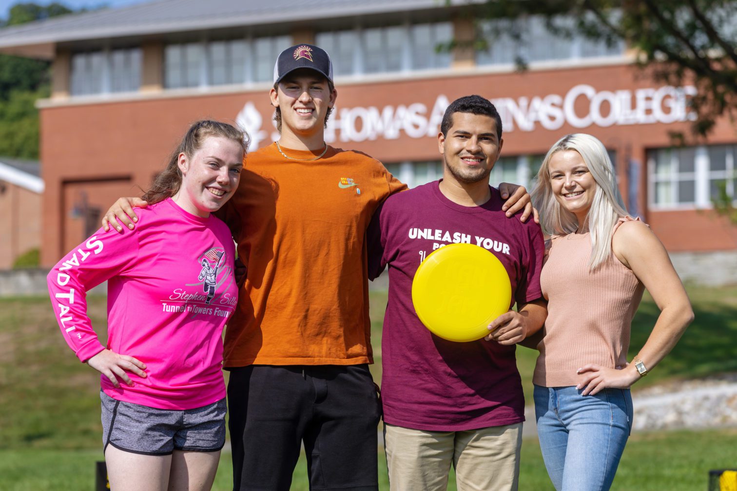 Four students, two male and two female standing. One male holding a yellow frisbee.