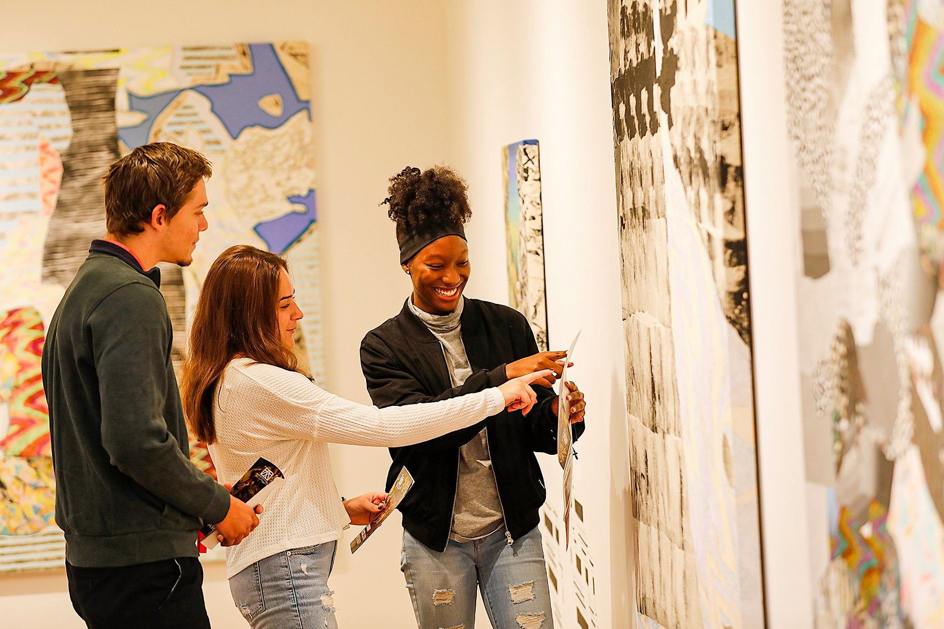 Three students looking at an art on the wall.