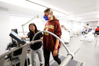 A student and her professor on the treadmill in the exercise lab and students sitting a a desk.