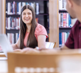 A male and female student sitting at desks in the library.