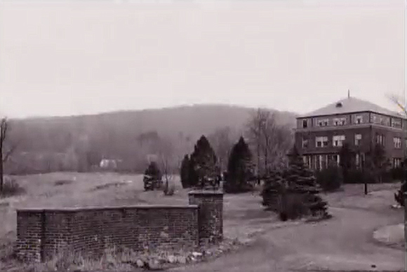 Old photo from 1952 of St.Thomas Aquinas College with brick wall at entrance to driveway and building in the background