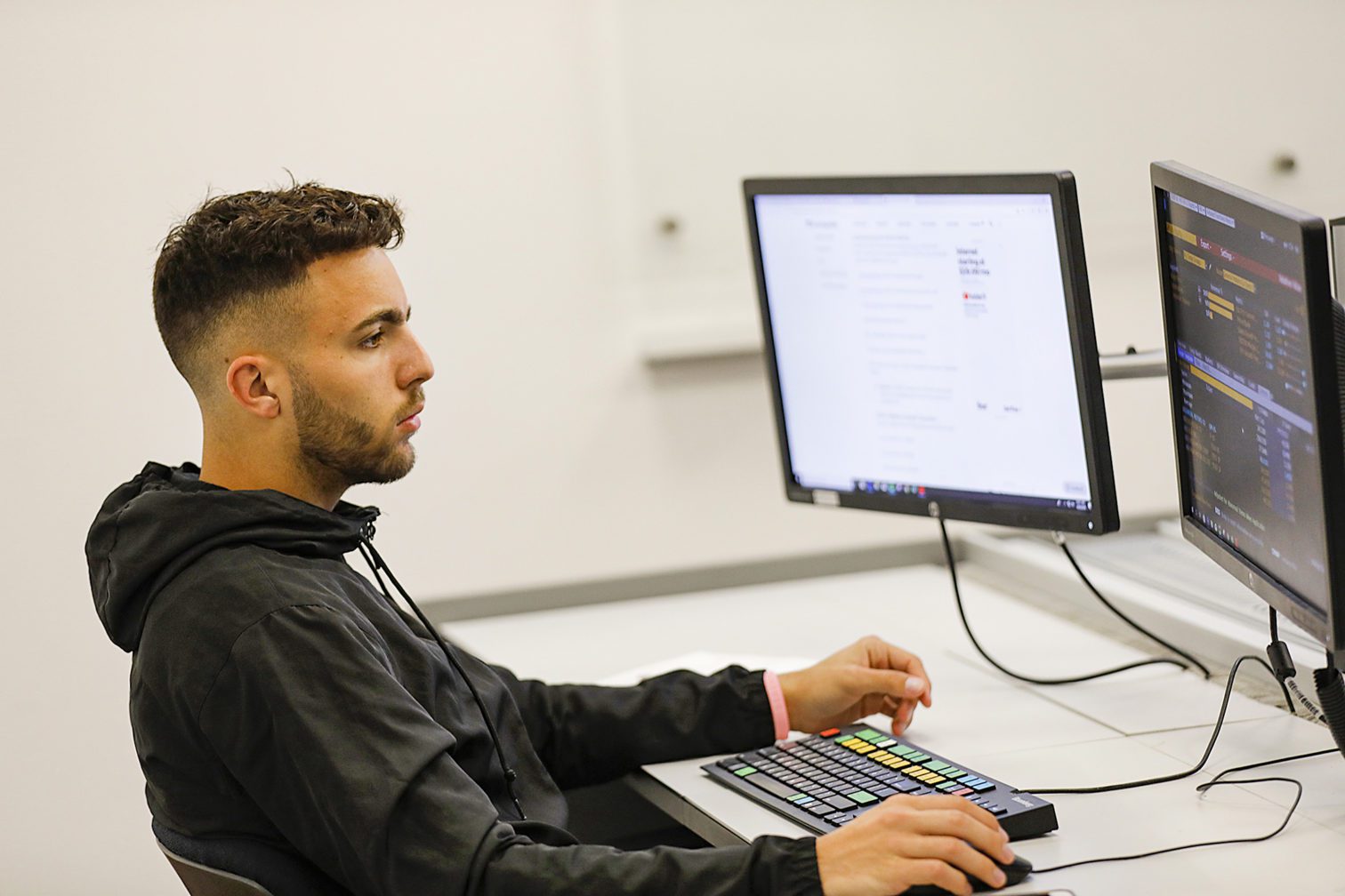 A male student sitting in front of a computer and holding the computer mouse.