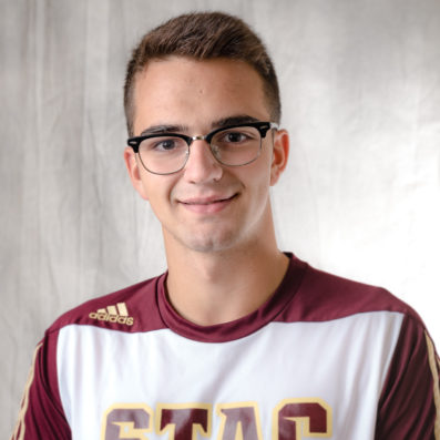 Andreu smiling wearing STAC athletics t-shirt and black-rimmed glasses