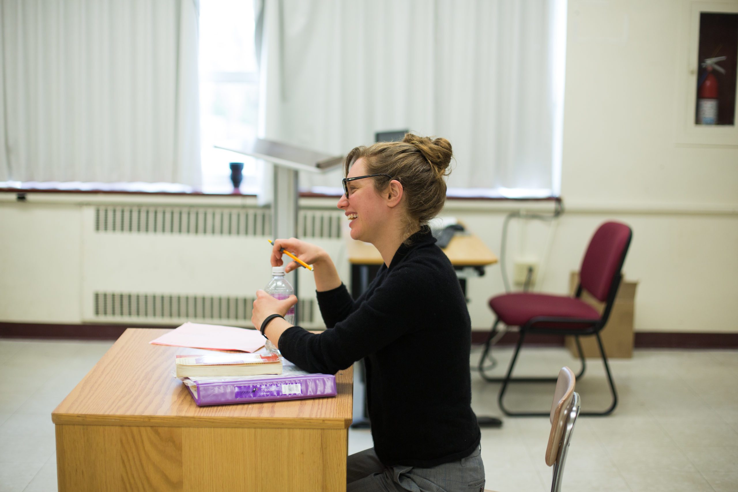 A female professor sitting at a desk in a classroom.