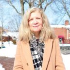 Dr. Finnegan smiling outside with snow in the background wearing beige coat and back and white scarf