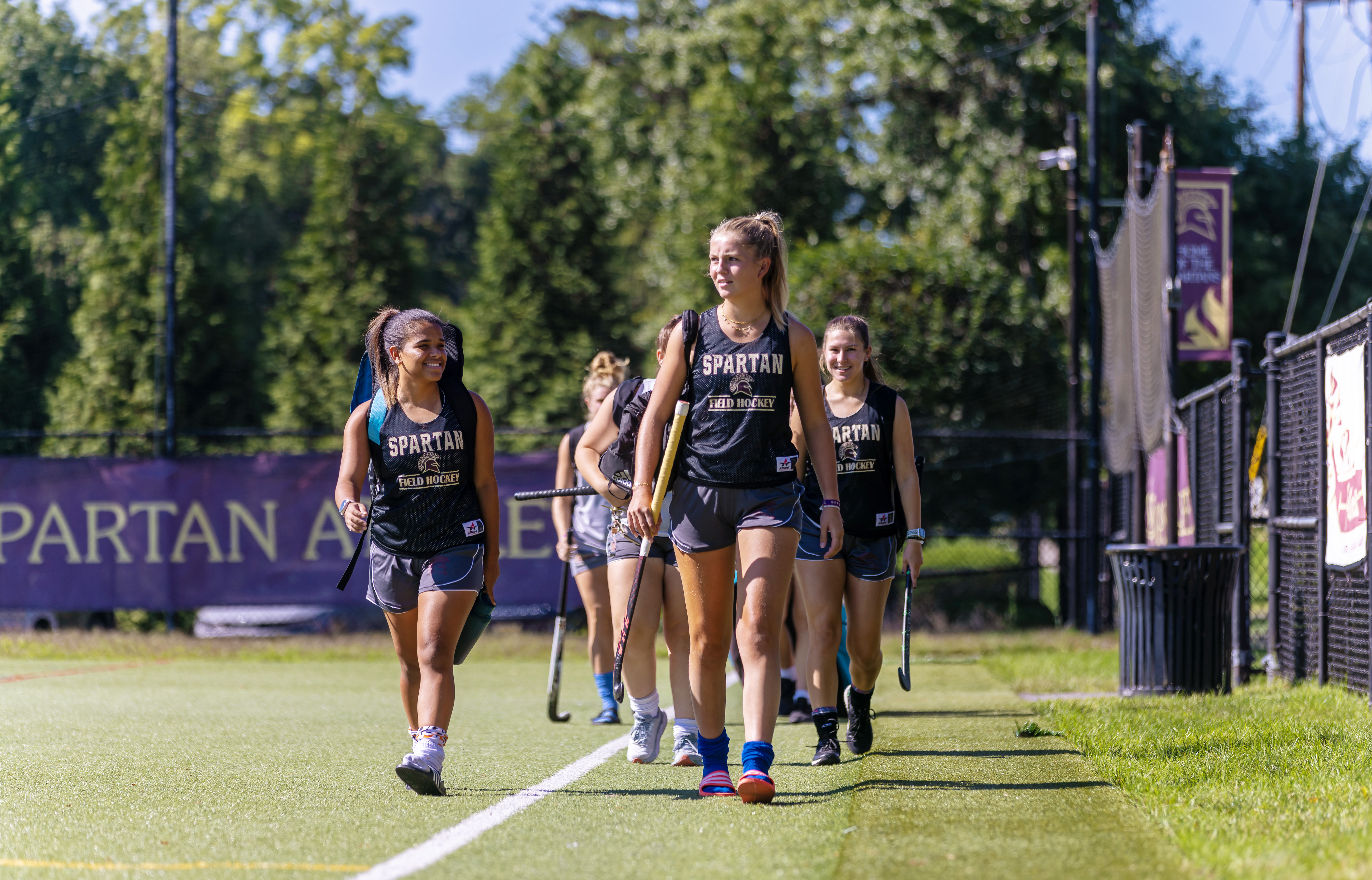 Female hockey players in gear walking on the field.