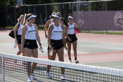 Female students in tennis gear walking on the tennis court.