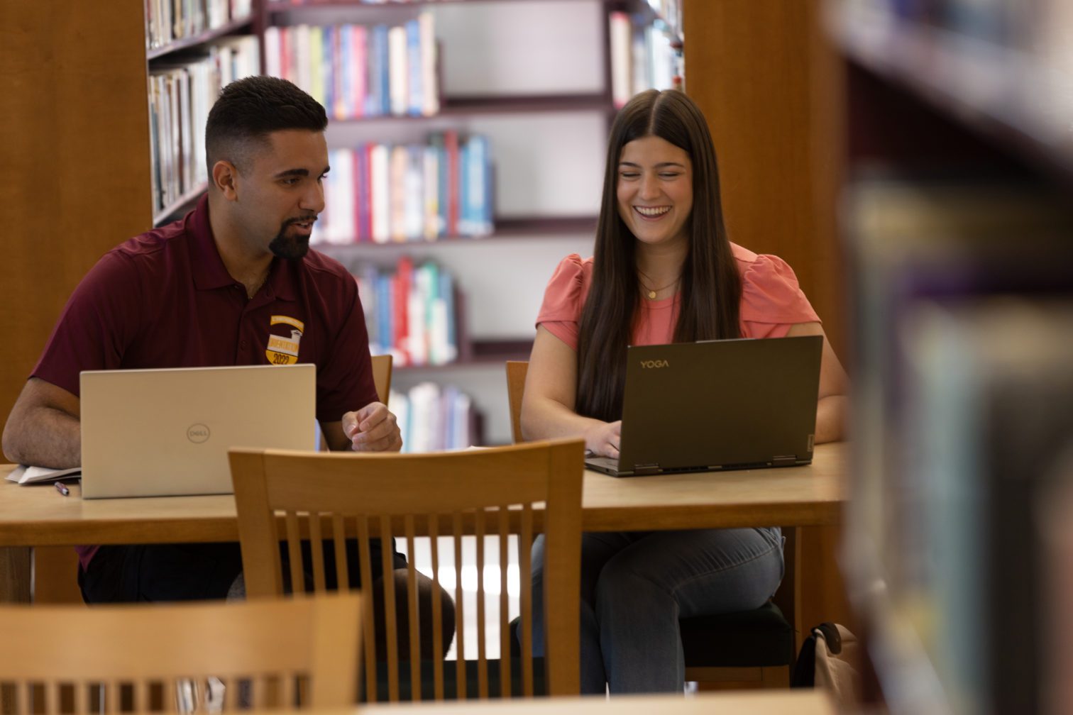 Two students sitting at desks in the library working on their laptops