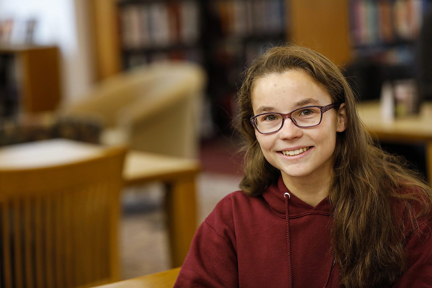 A female student with glasses sitting at a desk in the library.