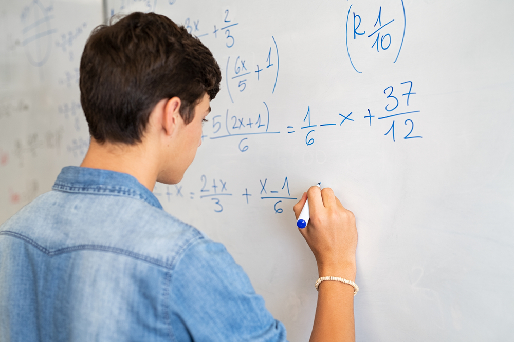 A male student solving a math equation on a whiteboard