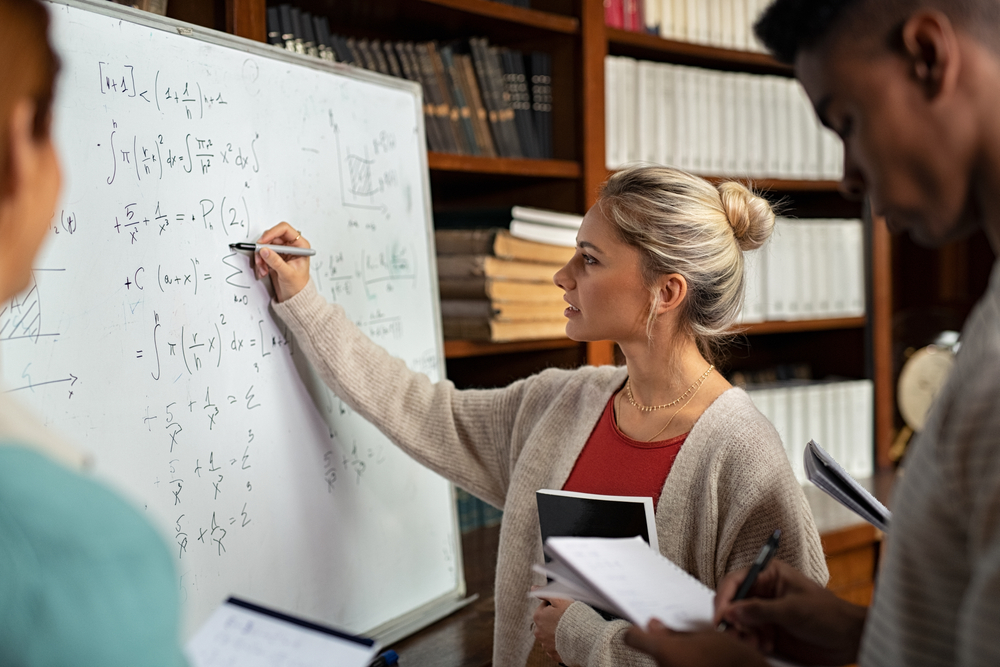 A young woman solving a math problem on a whiteboard