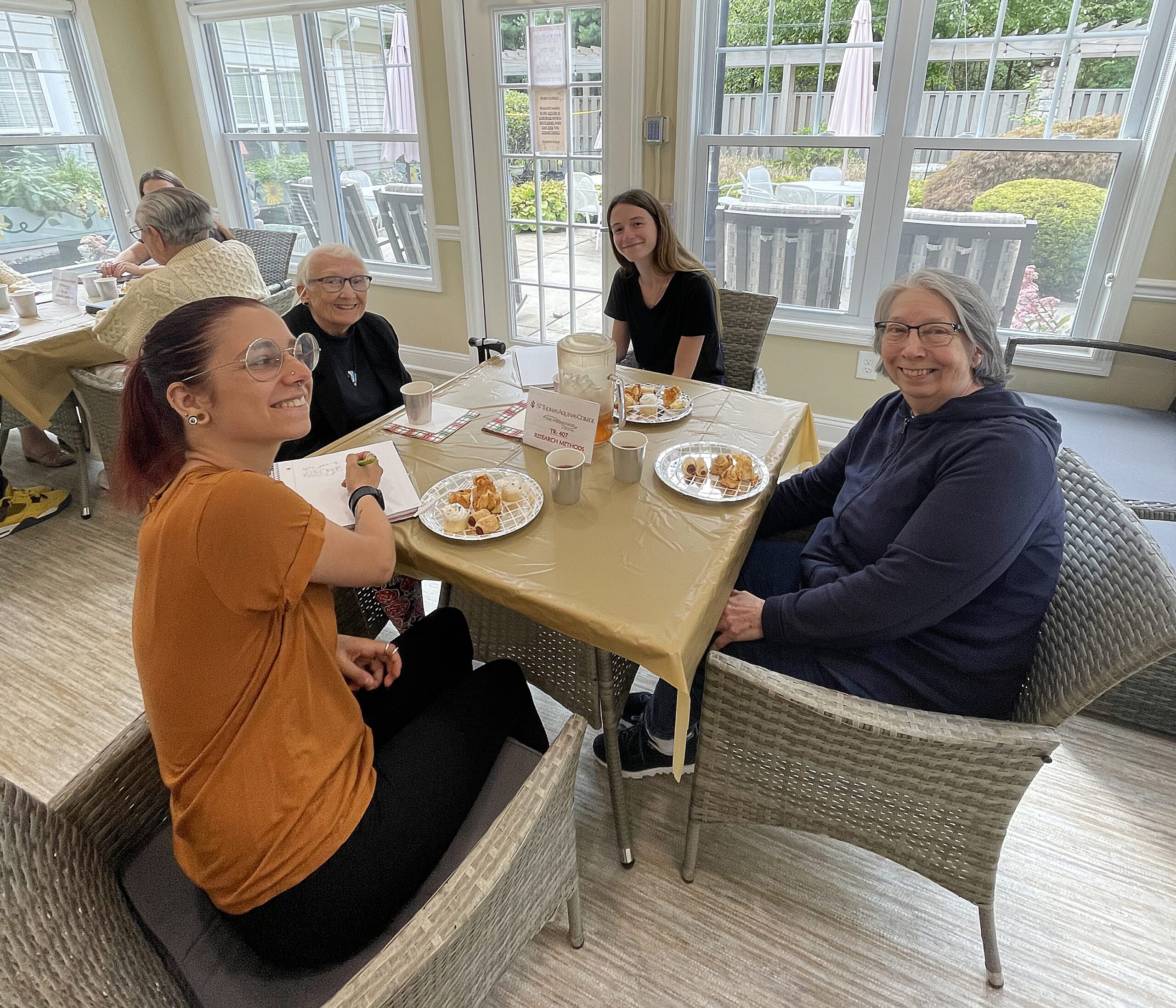 two students and two participants at assisted living center seated at table smiling enjoying food together