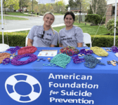 two individuals on campus seated at AFSP table with beads smiling
