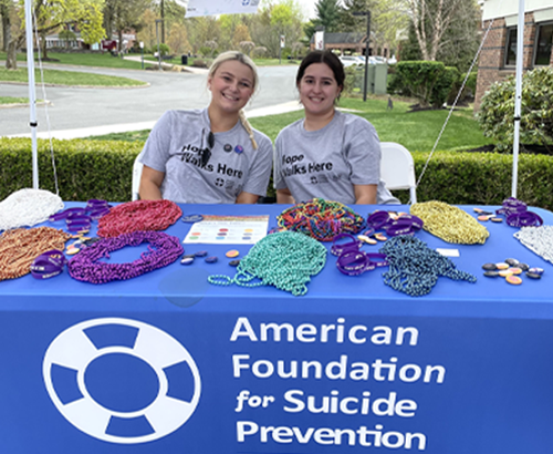 two individuals on campus seated at AFSP table with beads smiling