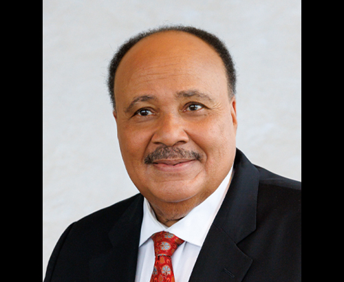MLK III head shot image smiling wearing black suit and red tie