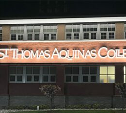 St. Thomas Aquinas College signage on Costello Hall building at night lit up with glowing white light.