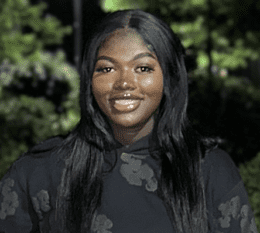 Fatima smiling wearing black sweatshirt with green trees in background