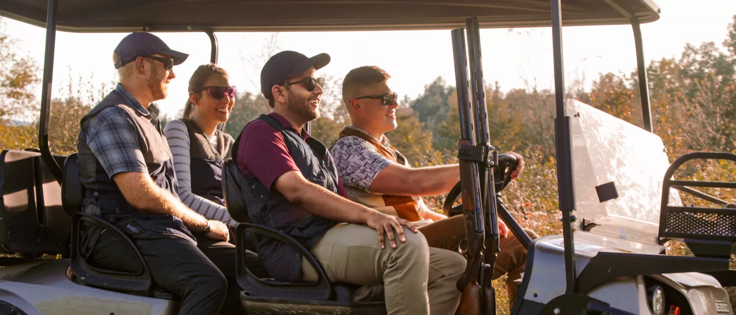 3 men and 1 women in a golf cart driving 