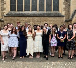 group of student studying in Oxford outside wearing formal attire smiling for photo. Oxford University building in background