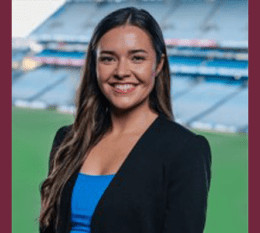 Mary Kate Henry smiling wearing black blazer and blue shirt with Stadium in background