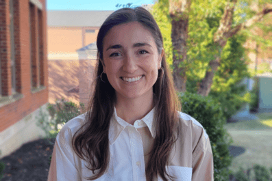 Sarah smiling with green trees and Borelli Hall and Romano buildings in background