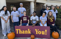 Students posing outside and smiling with thank you sign and pumpkins