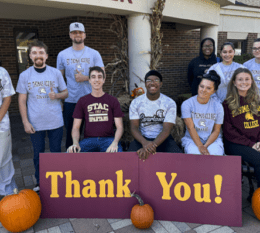 Students posing outside and smiling with thank you sign and pumpkins