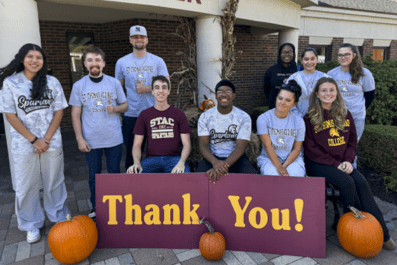 Students posing outside and smiling with thank you sign and pumpkins