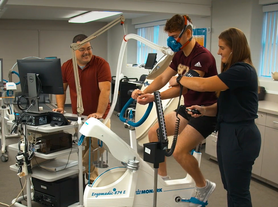 Professor and two sudents using exercise science equipment in lab on campus