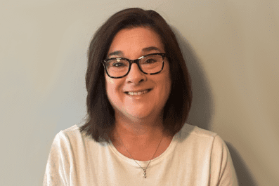 Lisa Horgan smiling wearing black rimmed glasses and cream colored shirt with drop necklace