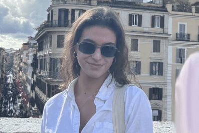 Sydney smiling wearing sunglasses with buildings and city streets of Rome in background